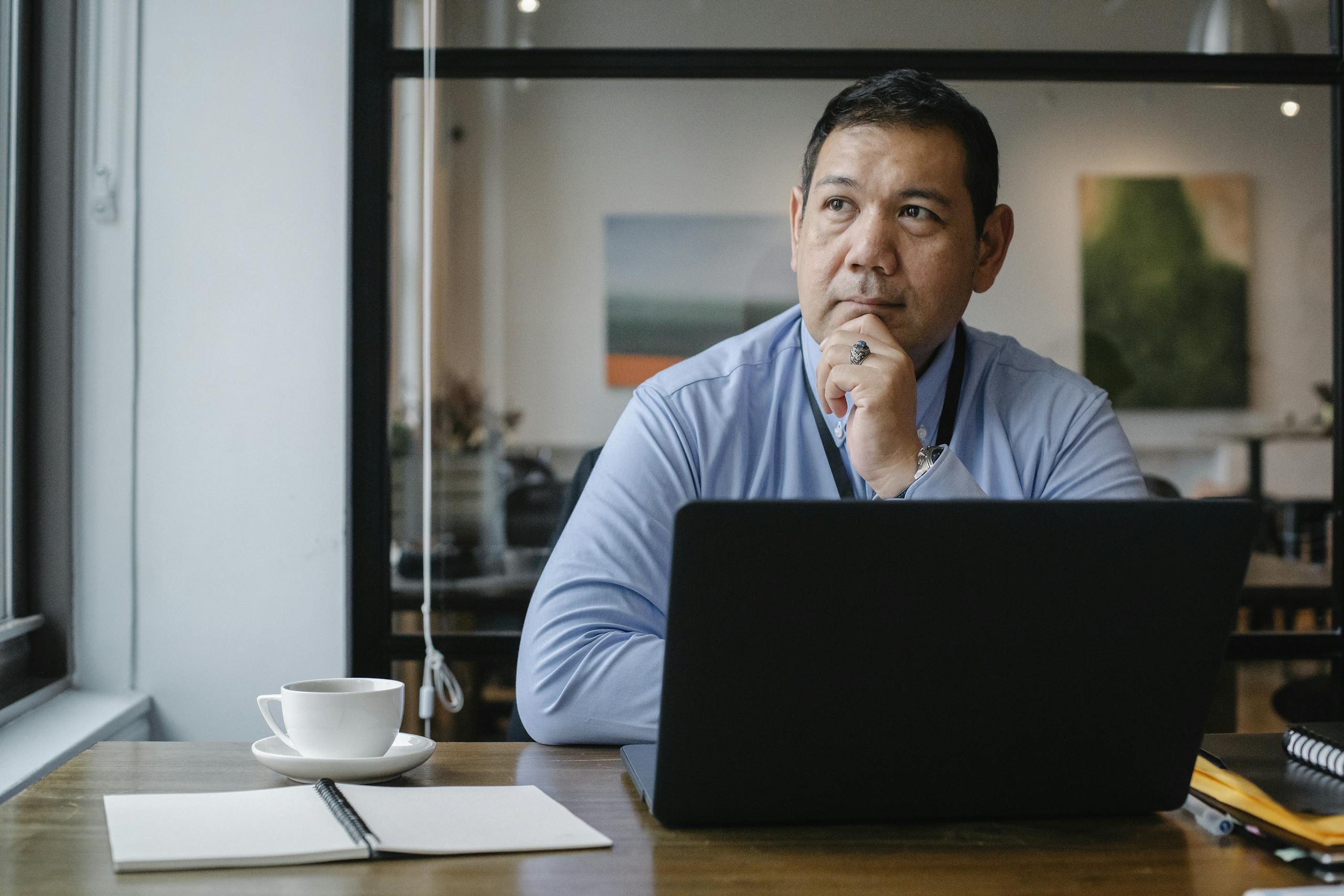 A businessman deep in thought while working on a laptop in a modern office setting.